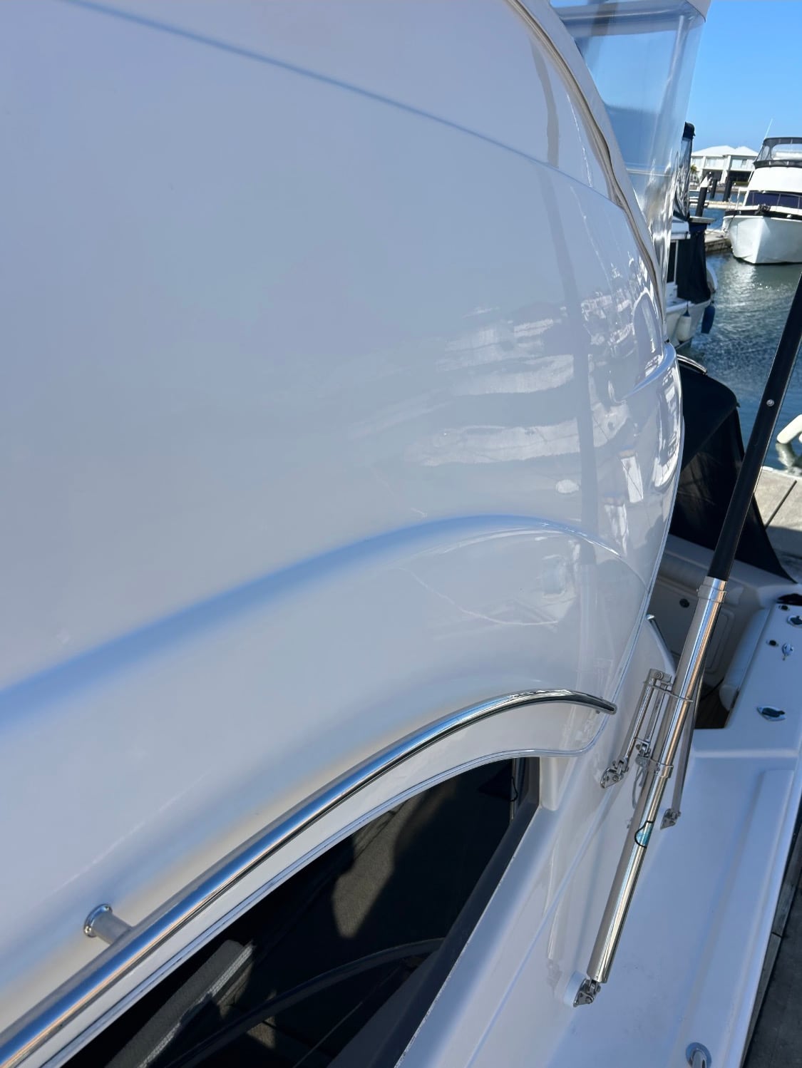 Cabin side and stainless grab rail before correction — the gelcoat flat and hazy, holding no reflection